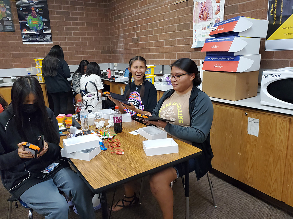 Two groups of students in a classroom open packages containing solar-powered battery banks which will allow them to charge their devices.
